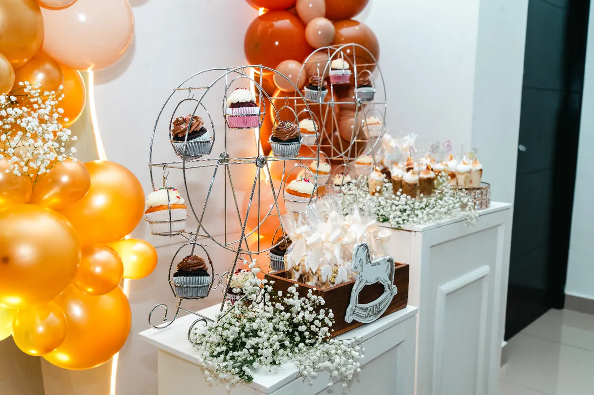 Rueda metálica de cupcakes rodeada de globos dorados y baby's breath